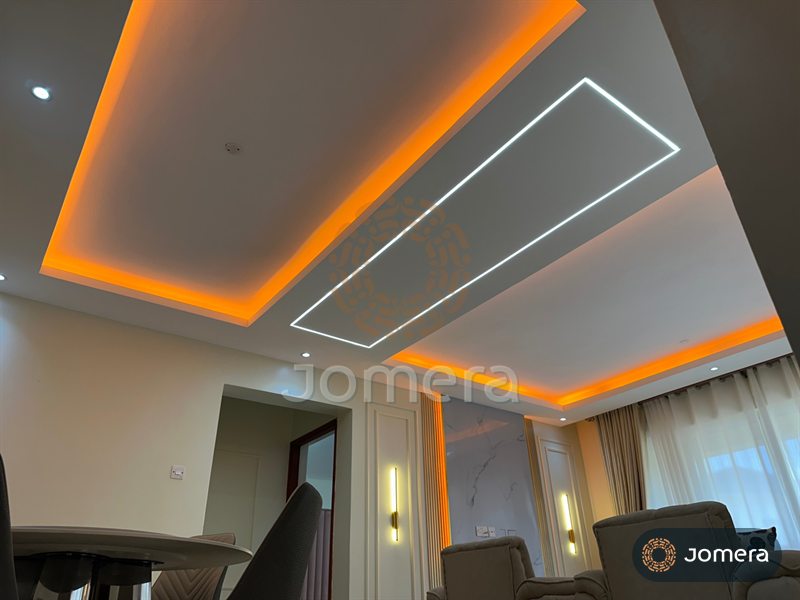 Upward view of a layered gypsum ceiling with warm cove lighting and an inset white linear light frame over a living and dining space