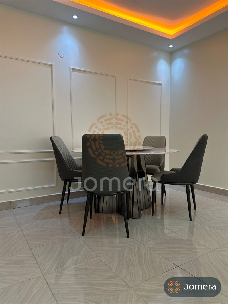 Dining corner with a round sintered-stone table on a mirrored pedestal, chevron-stitched dining chairs, wall mouldings and a warm-lit ceiling cove