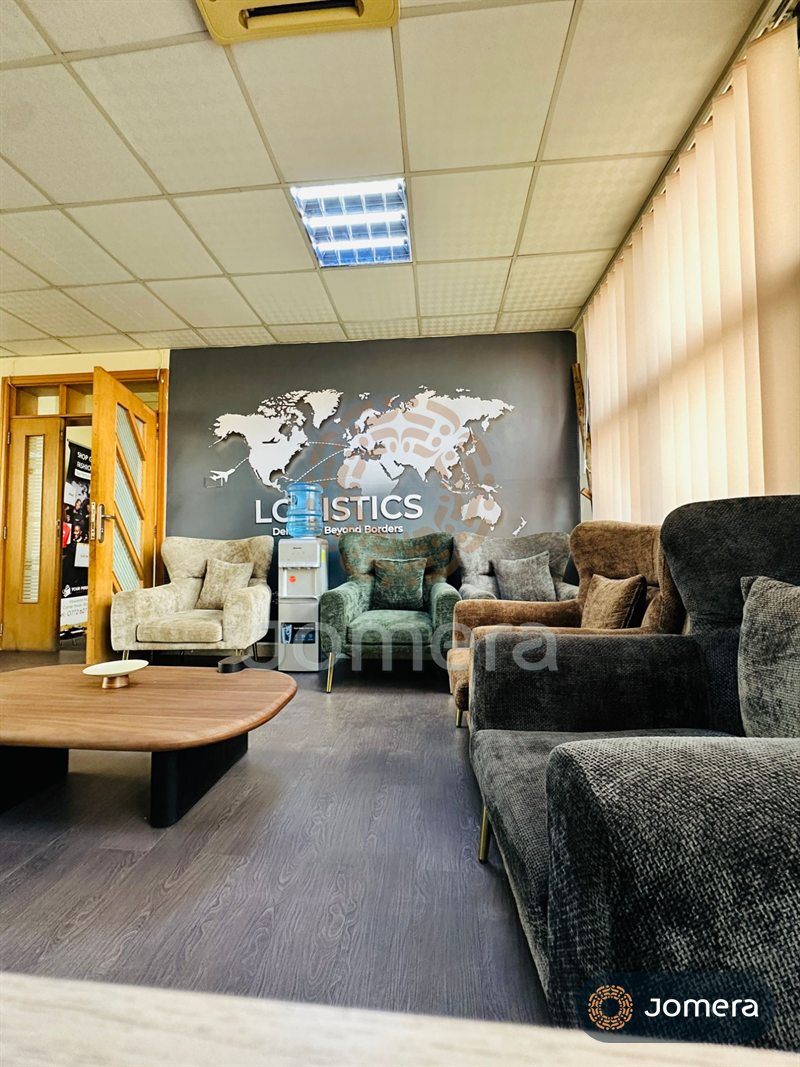Office client lounge with velvet wingback chairs in sage, oatmeal and cocoa, a low walnut coffee table and a world-map feature wall