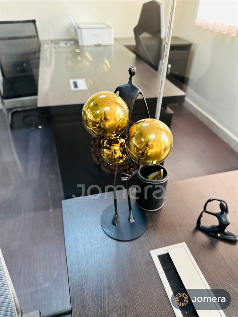 Close-up of an executive desk styled with a black metal figure sculpture holding mirrored gold spheres