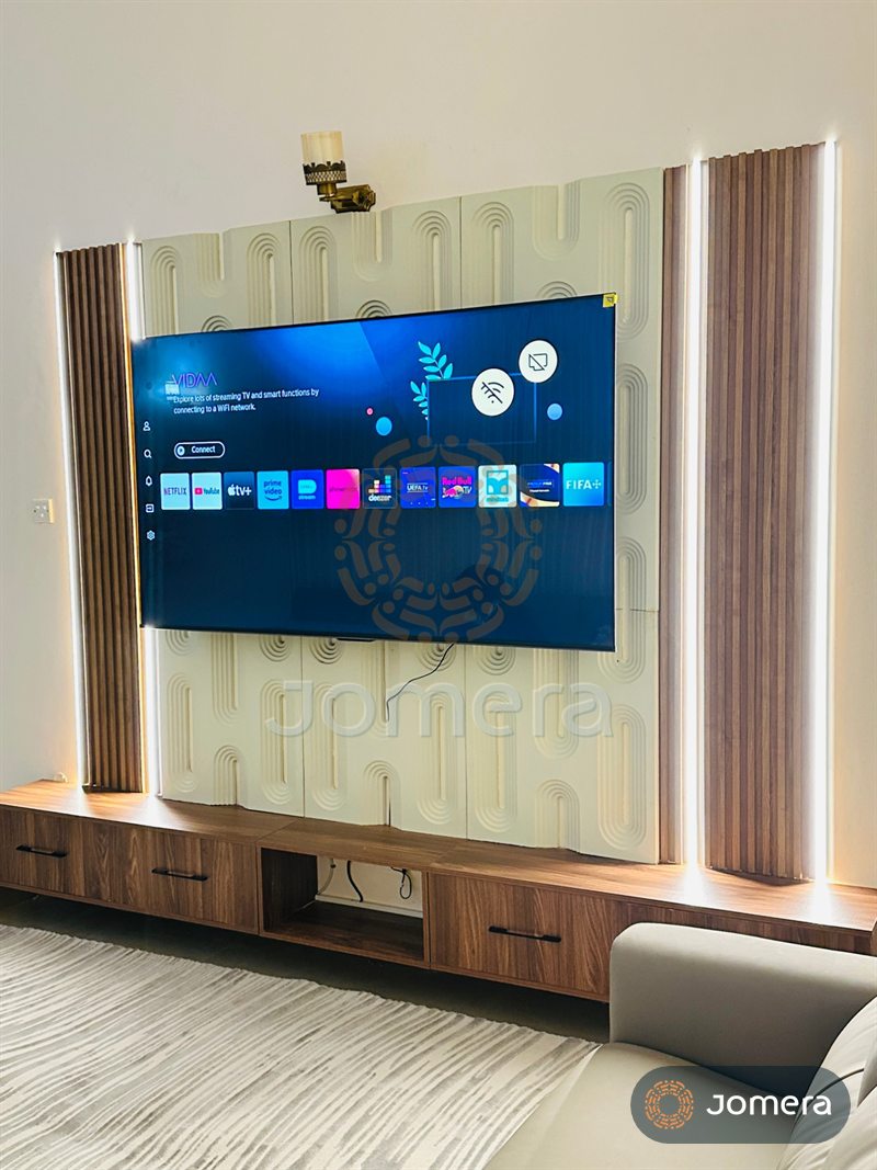 Angled view of a custom TV wall showing fluted walnut columns with LED strips beside sculpted arch-pattern panels above a floating media unit