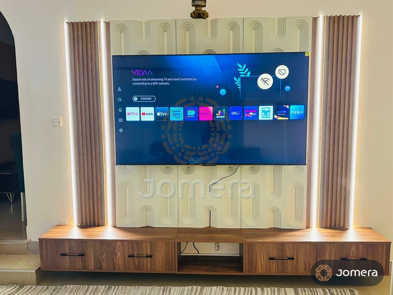 Custom TV wall with sculpted cream relief panels, fluted walnut columns edged in LED light and a floating walnut media unit